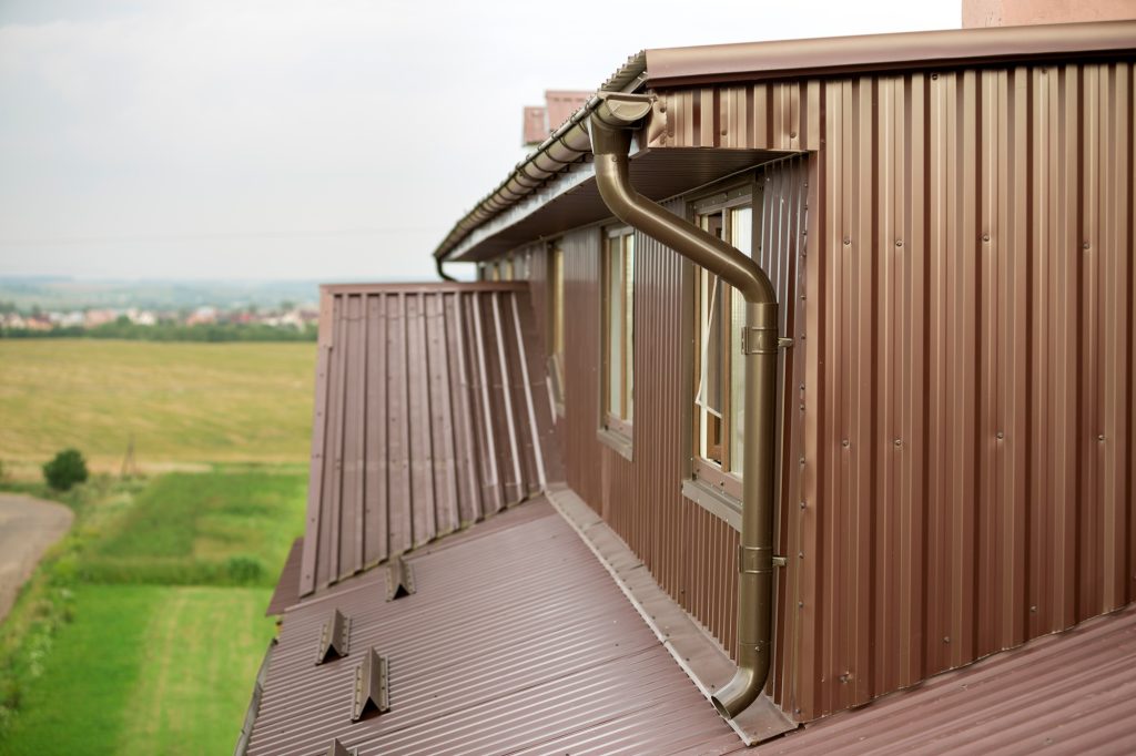 Cottage attic room, roof and walls covered with brown metal siding planks, new gutter system